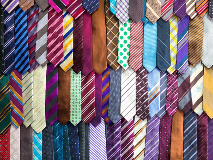 Ein buntes Sortiment an Krawatten in verschiedenen Mustern und Farben hängt geordnet an einer Wand.