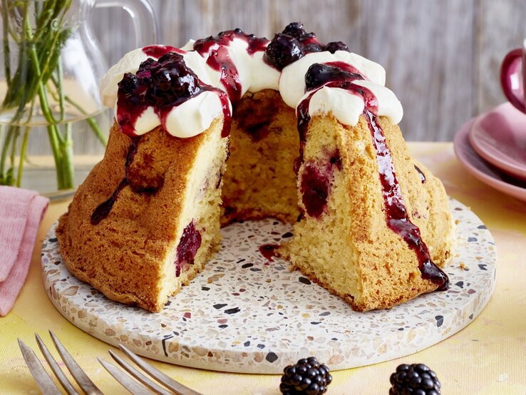 Brombeer-Apfel-Gugelhupf auf einem Tortenteller auf gelben Hintergrund. 