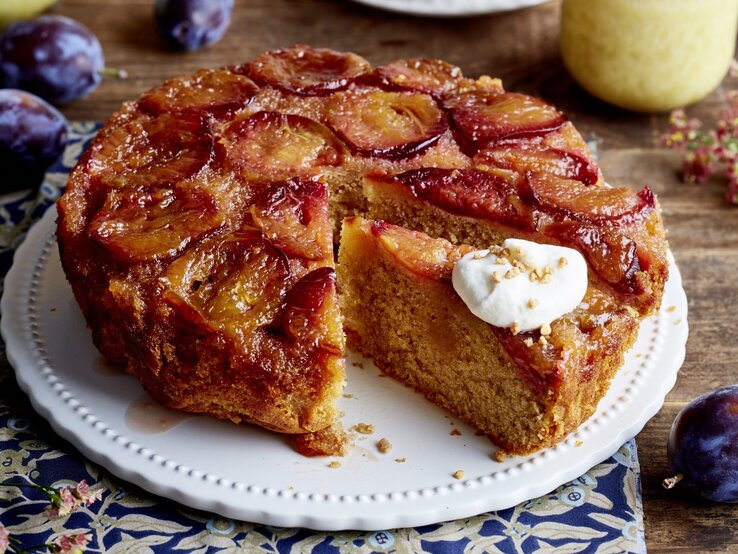 Karamell-Pflaumen-Kuchen auf einem weißen Tortenteller auf hölzernem Hintergrund. 