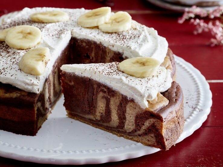 Zebra-Bananen-Kuchen angeschnitten auf einem weißen Teller auf rotem Hintergrund.