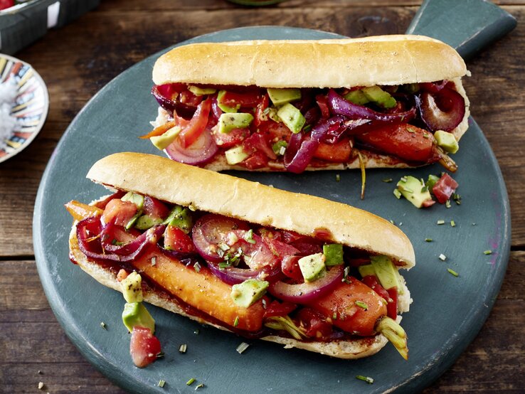 Hotdog mit Möhren und Salsa auf einem dunkelgrauen Teller auf hölzernem Hintergrund.