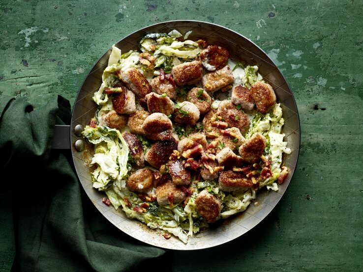 Gnocchi „Amore mio“ auf cremigen Wirsingstreifen in einer schwarzen Pfanne auf dunkelgrünem Hintergrund.