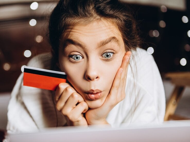 Eine Frau guckt entsetzt auf ihren Laptop und erkennt die Kostenfallen. Mit Kreditkarte in der Hand.