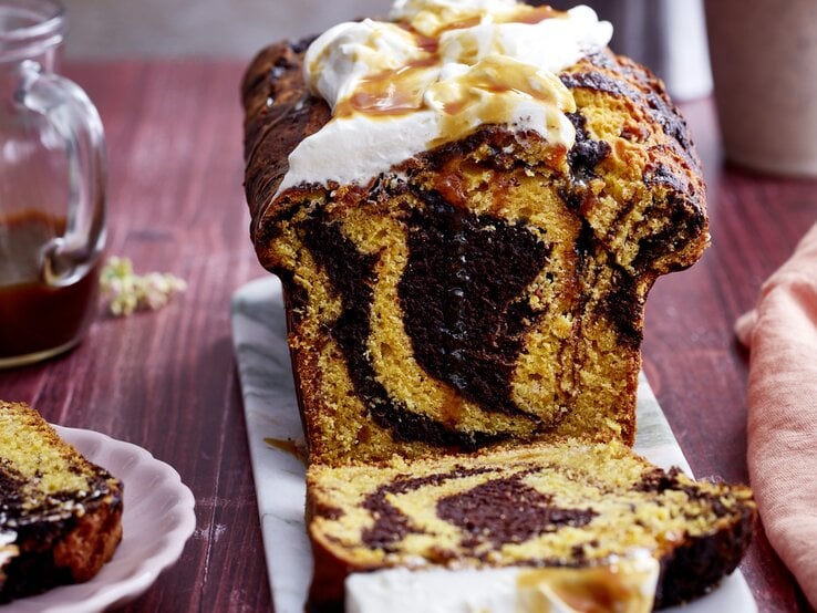 Kürbis-Kakao-Kuchen auf einem grauen Servierteller, auf dunkelrotem Hintergrund. 