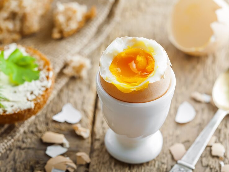 Wachsweich gekochtes Ei in einem weißen Eierbecher auf Holztisch. 