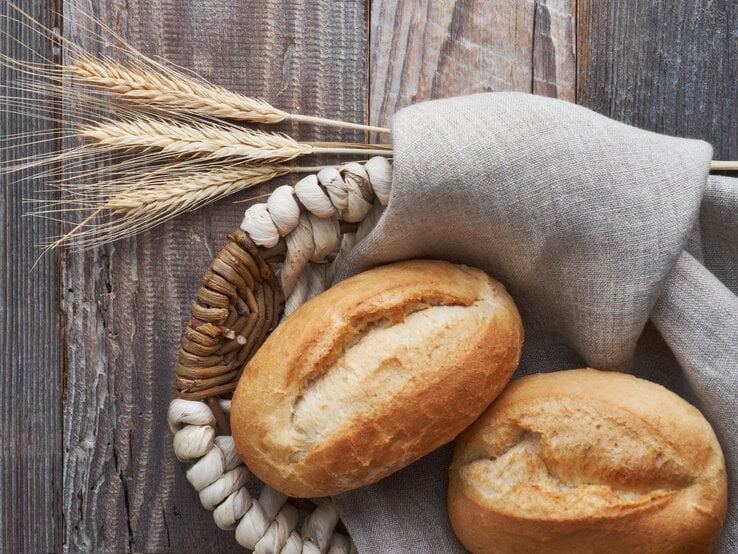 Zwei Brötchen im Brotkorb auf graubraunem Holz. 