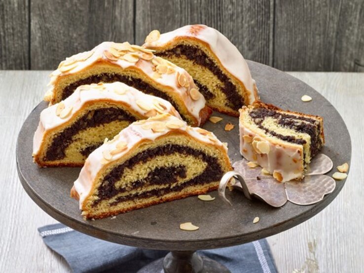 Mohnstollen auf einem schwarzen Tortenteller auf hölzernem Hintergrund. 