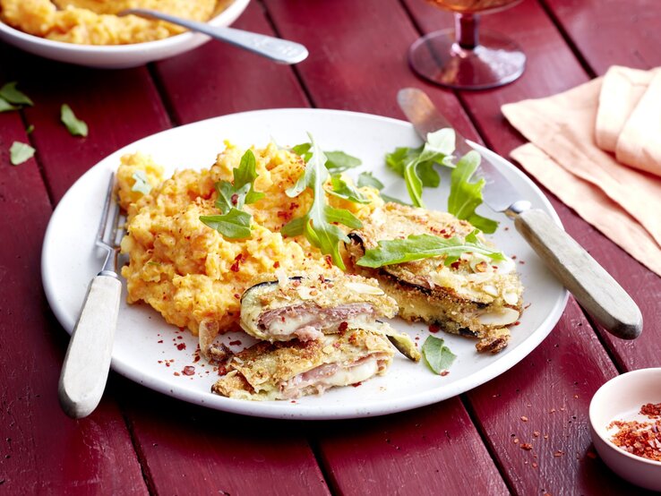 Auberginen-Cordon-Bleu auf einem weißen Teller auf dunkelrotem Hintergrund.