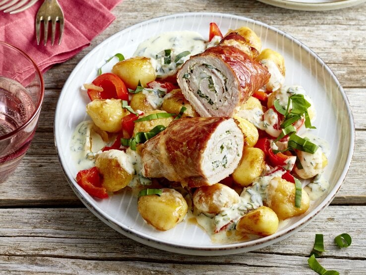 Bärlauch-Schnitzelröllchen auf einem weißen Teller auf hölzernem Hintergrund. 